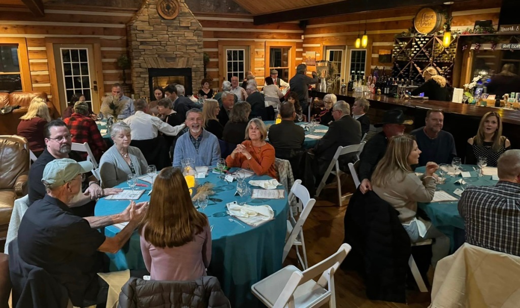 people sitting around tables with teal-blue tablecloths in the tasting room; fireplace in the background