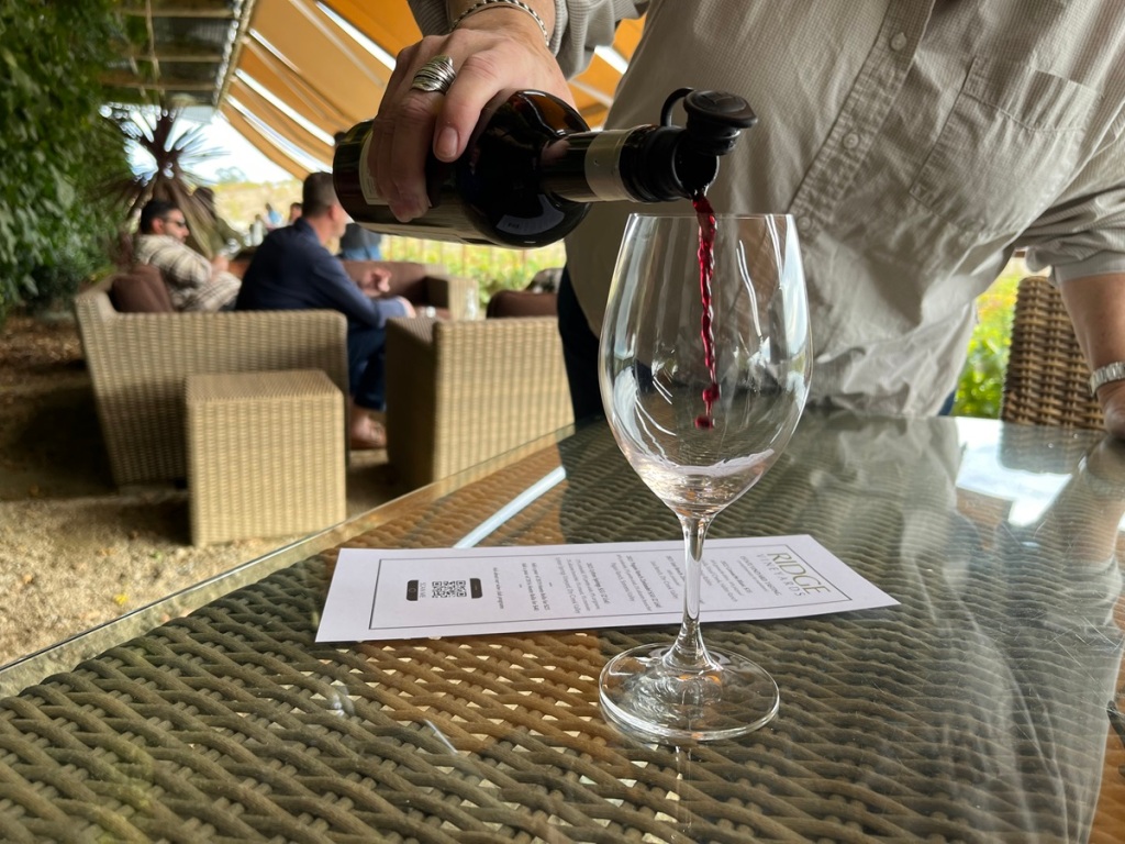 wine glass on table, with person pouring red wine from bottle into it
