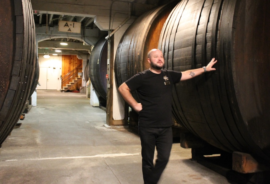 man leans against enormous wooden "barrel," with others in the background