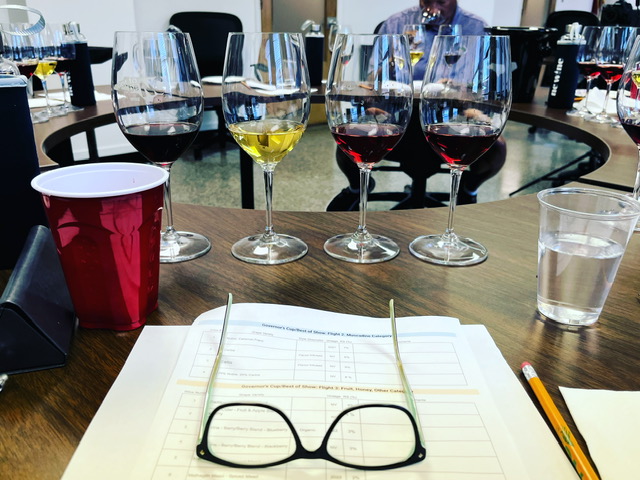 pair of eye glasses sits on a sheet of paper, with four wine glasses and wine in the background